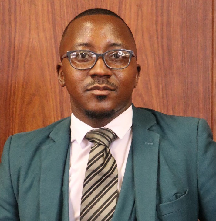 Black man with glasses wearing a suit with wooden background